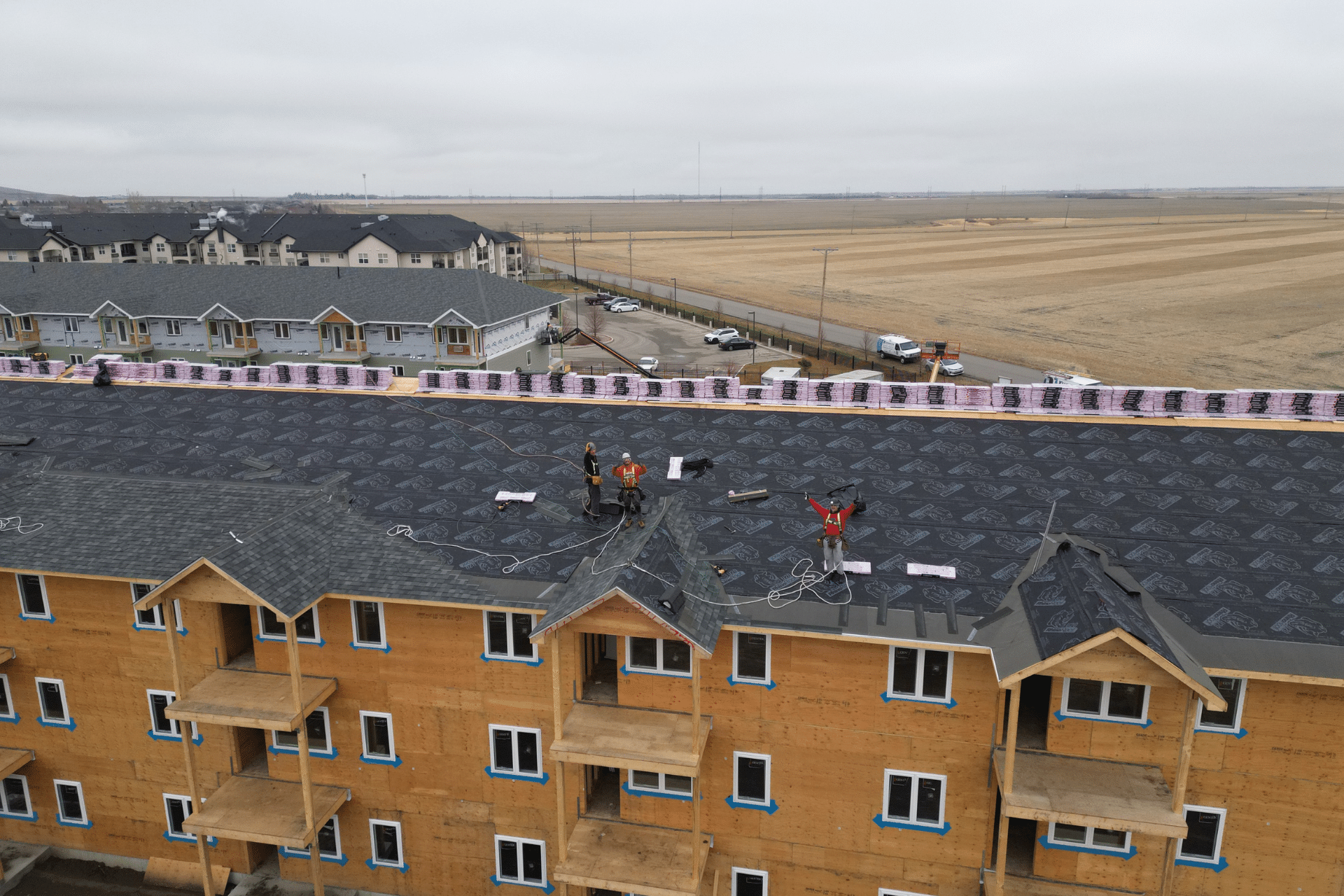 alt="Roofers working and waving from the top of a multi-unit building under construction, captured by drone in regina"